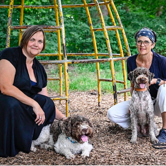 Zwei Frauen posieren mit ihren beiden Hunden auf dem Schulhof-Spielplatz.