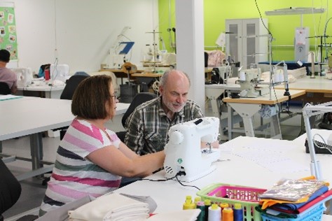 Eine Frau sitzt zusammen mit einem Mann an einer Nähmaschine und näht. Die Nähmaschine befindet sich in der Näherei der Werkstatt der Pestalozzi-Stiftung.